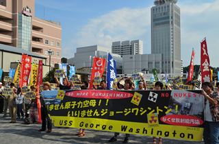 「原子力空母いらない！」「沖縄連帯！オスプレイＮＯ」と書かれたプラカードを掲げる集会参加者